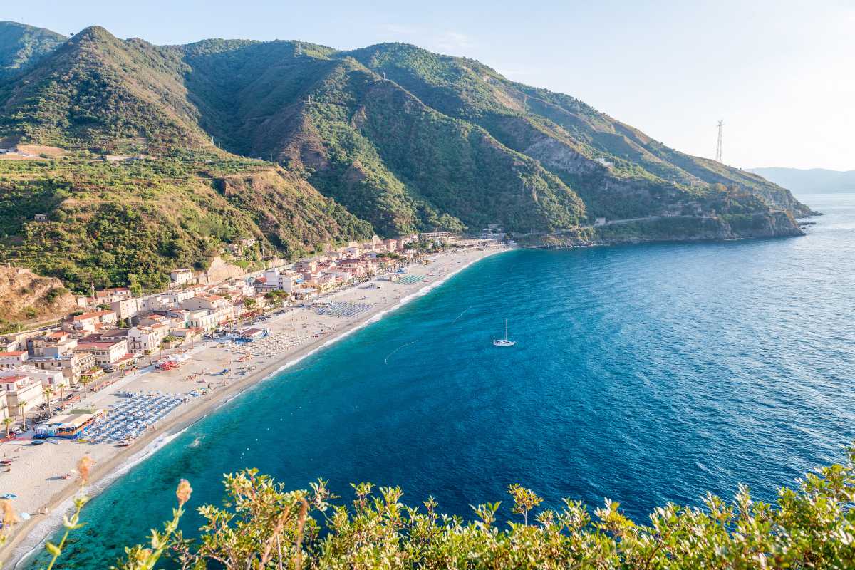 Un'auto parcheggiata con vista sul mare e il Castello di Scilla sullo sfondo.
