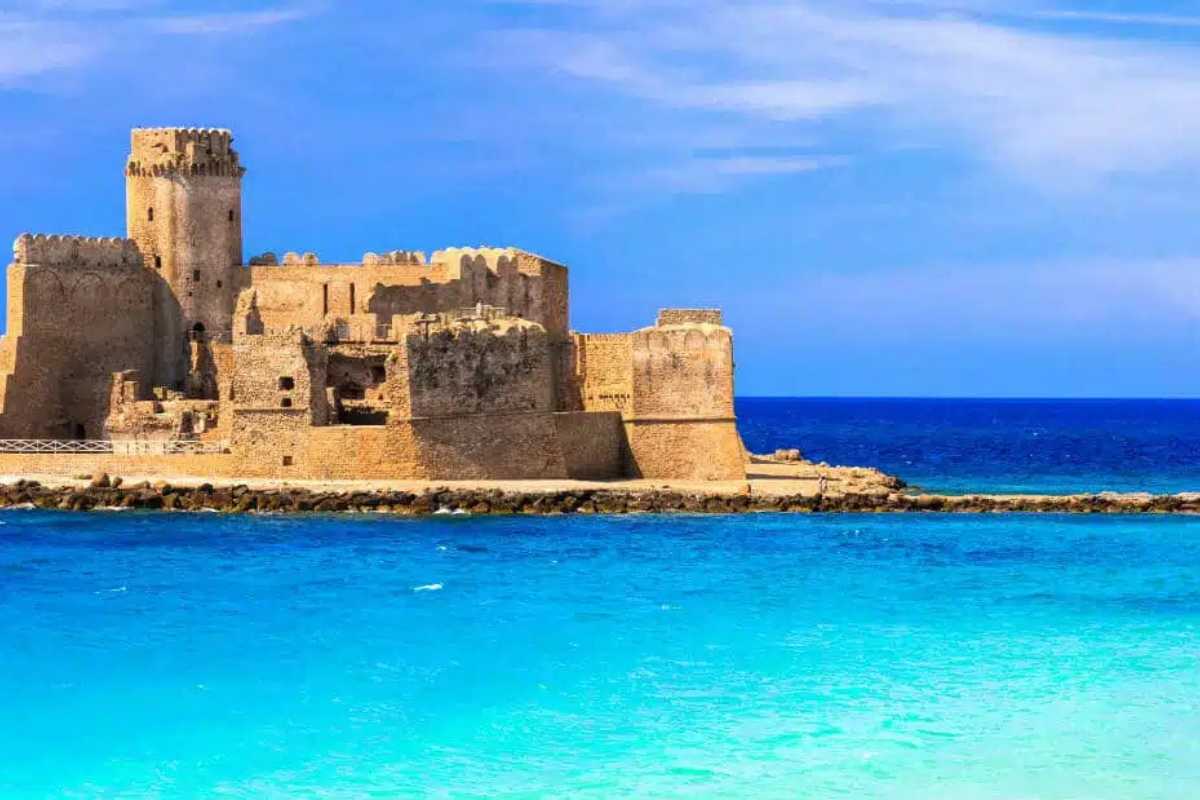 Fortezza aragonese vista dal mare, con sfondo del cielo azzurro e onde che si infrangono